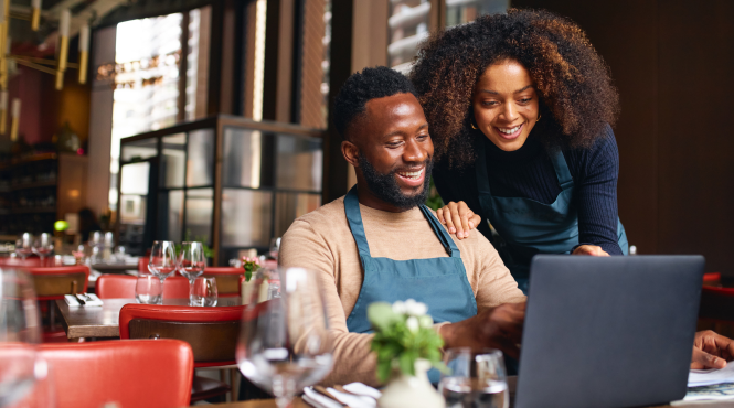 A male and female business owner sit in the dining room of their restaurant looking at the #smallbusinesseveryday digital tools for business owners.