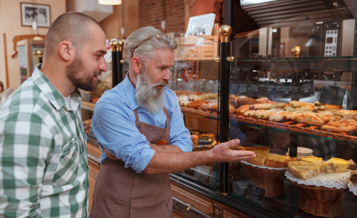 the proud owner of a local bakery showing a customer an assortment of baked goods in a display case including quiche, scones, and pastries. 