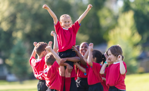 a local children's soccer team lifting one of their players into the air and celebrating their big win by cheering enthuiastically