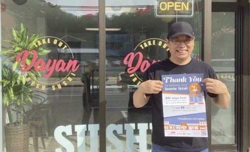 The owner of Dayan Sushi, a CFIB member in  Nova Scotia, standing outside his restaurant holding CFIB's Local Impact Poster and smiling.