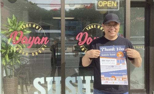 The owner of Dayan Sushi, a CFIB member in Nova Scotia, standing outside his restaurant holding CFIB's Local Impact Poster and smiling.
