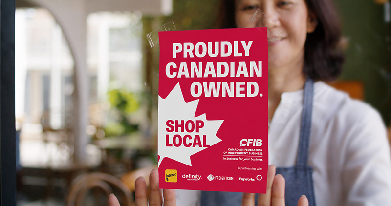 woman putting up a proudly Canadian owned poster in a storefront window