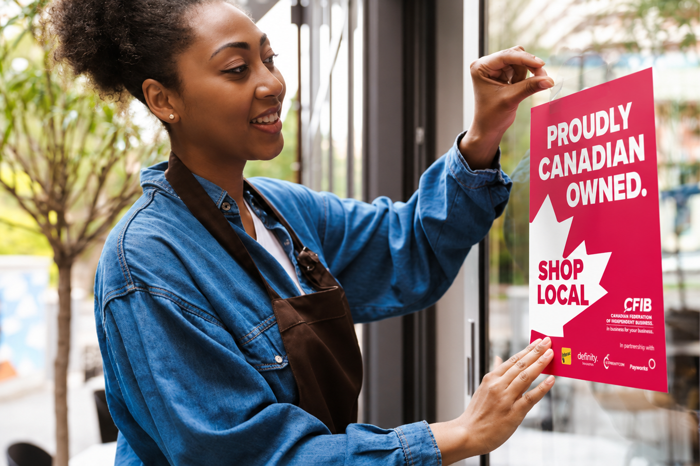 women putting a proudly Canadian owned poster up on a storefront window